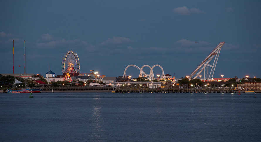 Wide bay view of boardwalk and tall amusement rides lit up at dusk
