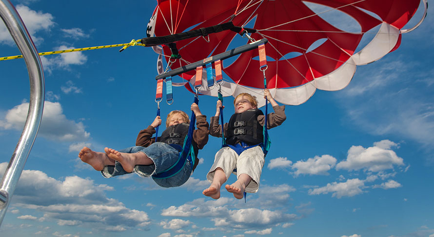 2 young boys parasailing into the partly cloudy blue sky